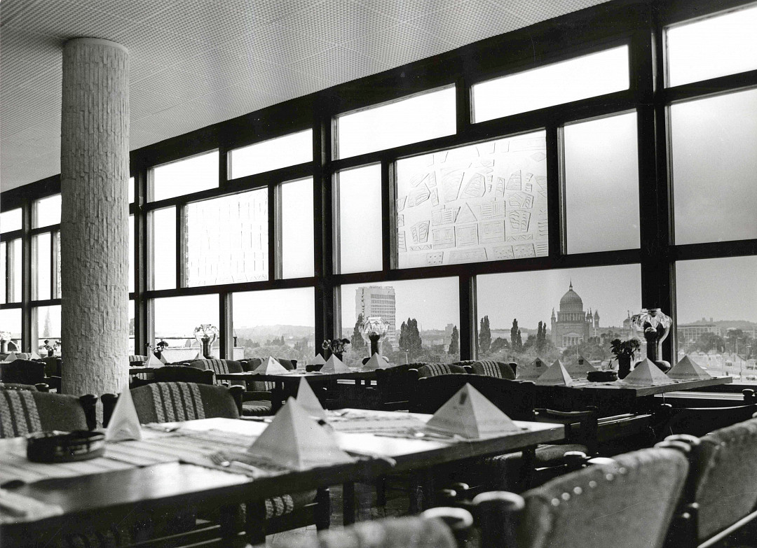 Black and white photo of the dining room of the former Minsk with set tables but still empty upholstered chairs. Tall windows open up a wide view over Potsdam.