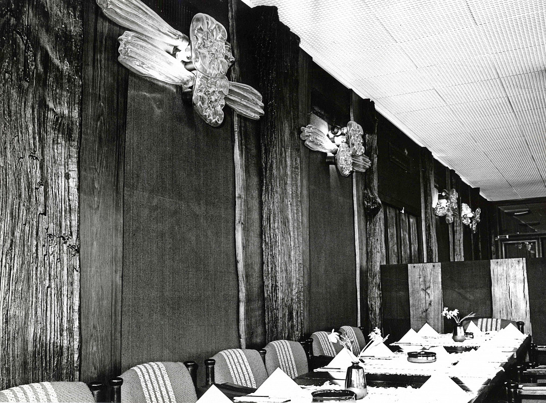 Black and white photo of the interior of the former Minsk restaurant with set tables but no guests yet. Wide wooden panels and wooden designs decorate the wall.